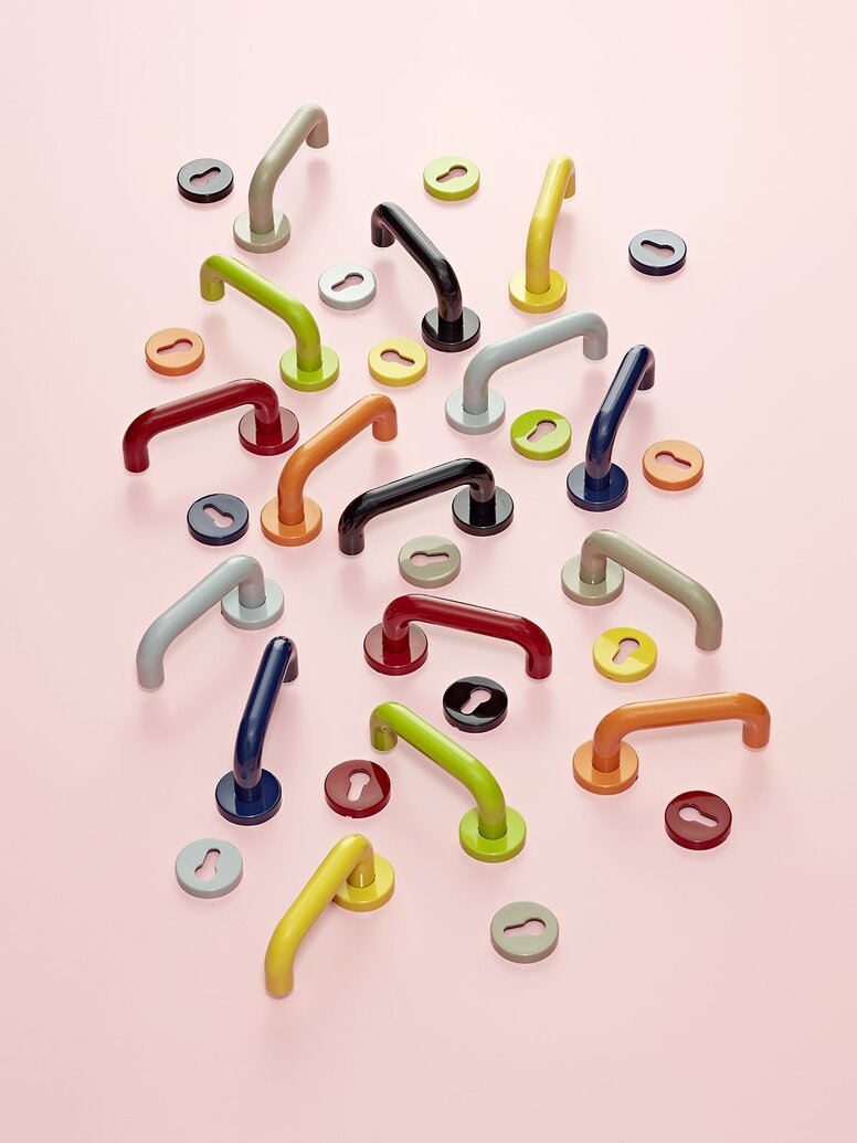 Künstlerische Ausstellung von 16 Türdrückern und Schlüsselrosetten System 111 in 8 verschiedenen HEWI Farben auf pinkem Hintergrund