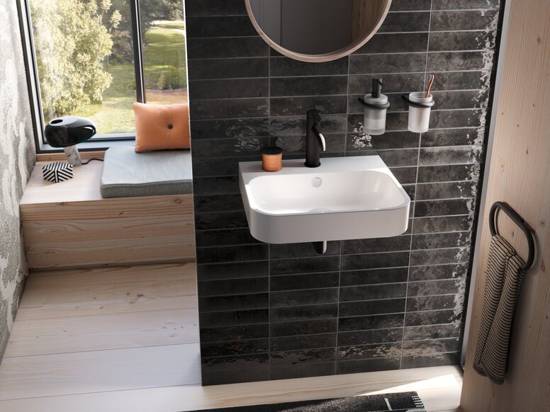 HEWI Fittings AQ Washbasin A white washbasin with a black tap and two wall-mounted cups on a black tiled wall in the wash area, set against a backdrop of black tiles