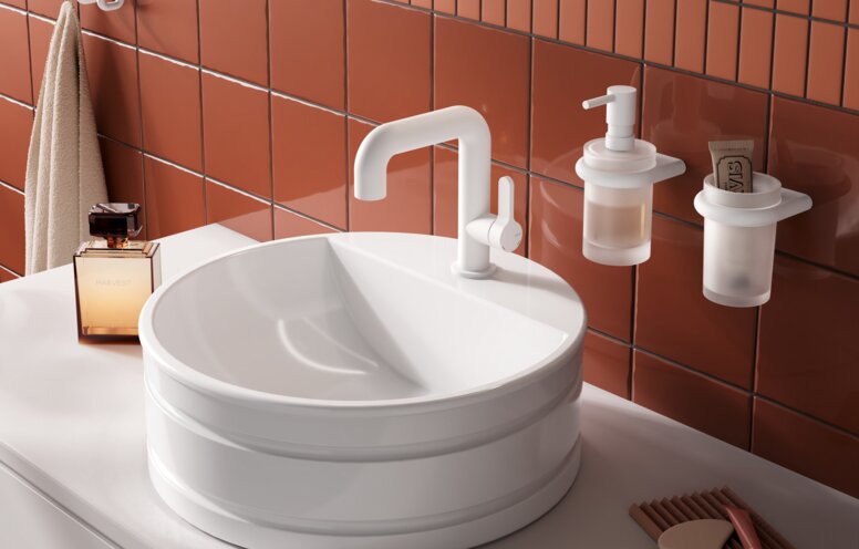 A round white countertop washbasin with a raised rim and a white tap, set on a light-coloured countertop against a backdrop of terracotta tiles