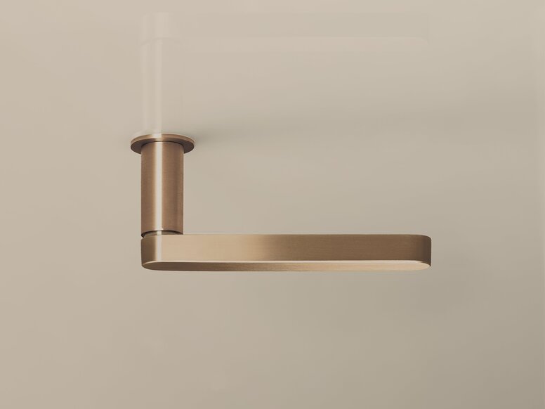 Copper-effect door handle with a round rose and a flat handle on a beige-coloured wall
