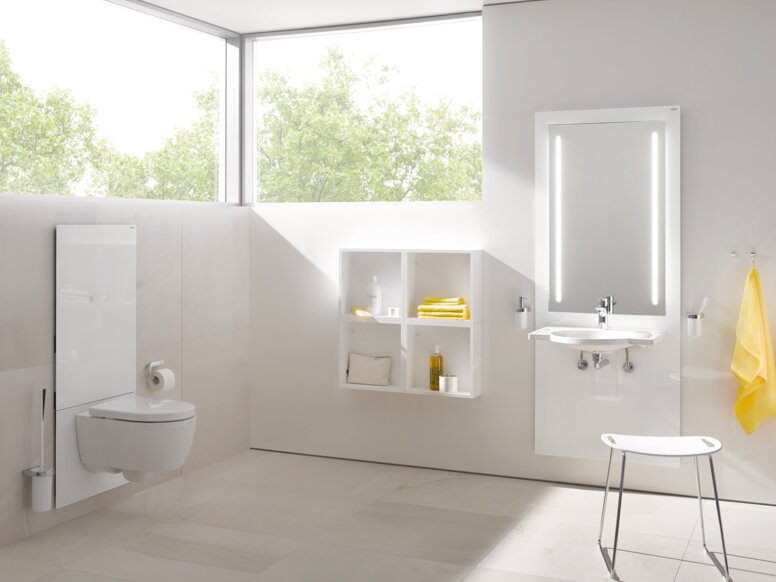 HEWI S 50 WC-Modul Weißes WC-Modul in einem hellen Badezimmer mit beleuchtetem Spiegel über dem Waschbecken, davor ein Hocker mit weißer Sitzfläche