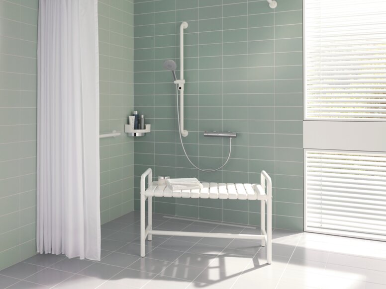 HEWI Range 801 Shower Bench for People with Obesity White shower bench with armrests and a shelf in the shower area against a light green tiled wall