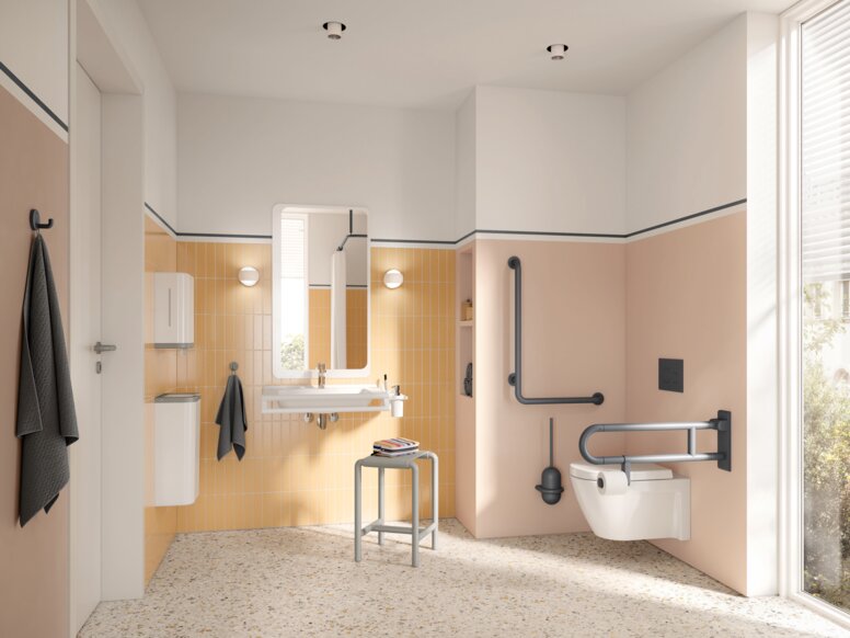 Wall-hung WC with a hinged support rail on the side and an L-shaped support rail, alongside a washbasin with a mirror and a stool