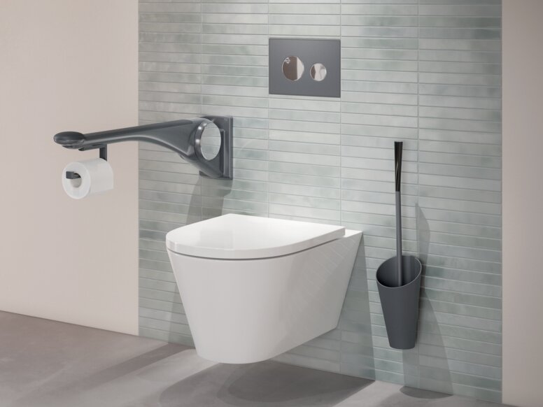 Wandhängendes WC mit seitlichem Haltegriff, integriertem WC-Papierhalter sowie einer an grüner Fliesenwand montierten Toilettenbürste