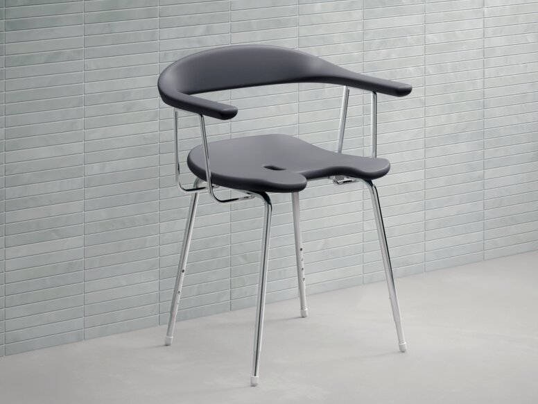 HEWI Range 802 LifeSystem premium shower stool Shower chair made of dark grey synthetic material with a semi-circular backrest, armrests and chrome-plated legs against a light grey tiled wall