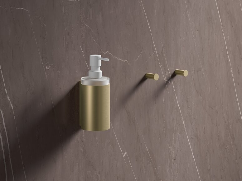 HEWI System 900 PVD soap dispenser with holder and single hook Brass-coloured PVD soap dispenser attached to a brown marble wall with two hooks