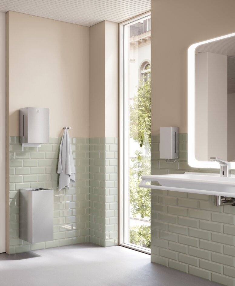 HEWI System 900Q Interior WC with toilet roll holder, support rail and toilet brush in a bathroom with light green tiles and a beige-coloured wall