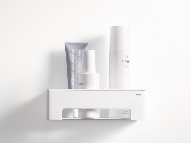 HEWI System 900 Duschkorb Weißer wandhängender Duschkorb mit Ablagefläche und offenem Fach, bestückt mit Pflegeprodukten an weißer Wand
