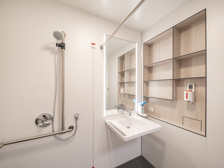 Patientenbad mit Waschplatz und Duschbereich ausgestattet mit HEWI Waschtisch und Brausehalter in Edelstahl